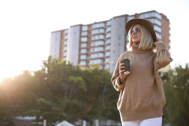 Photo of Woman in stylish sweater with cup of coffee on city street