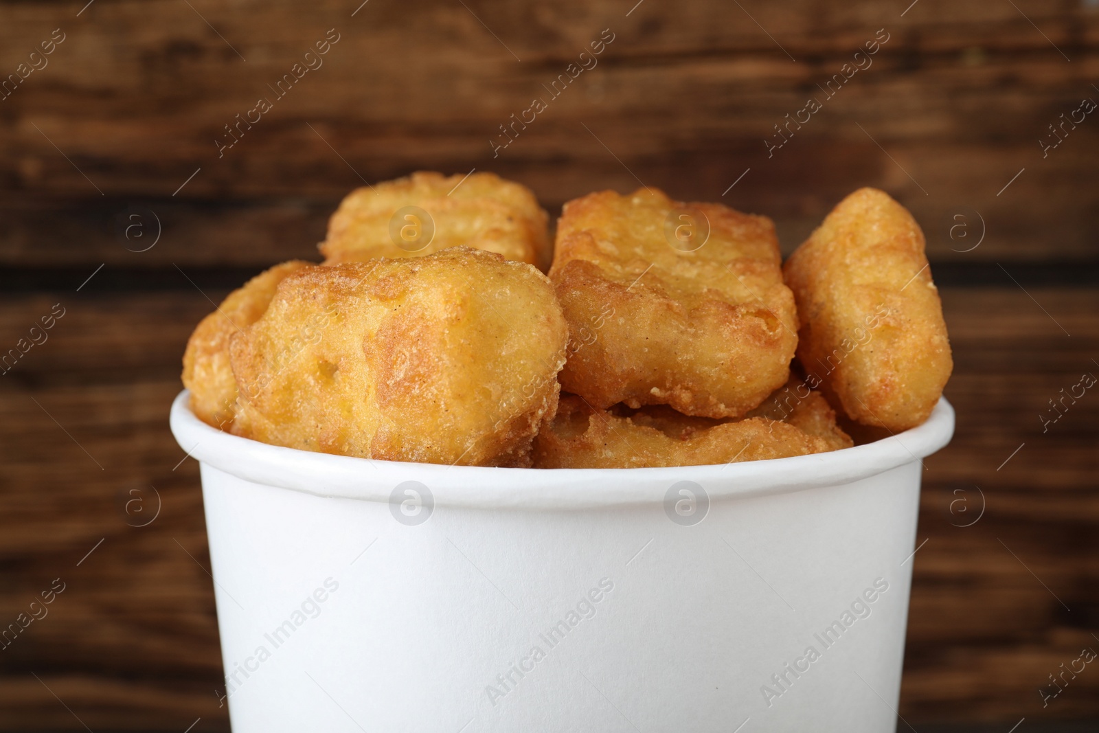 Photo of Bucket with tasty chicken nuggets on wooden background, closeup