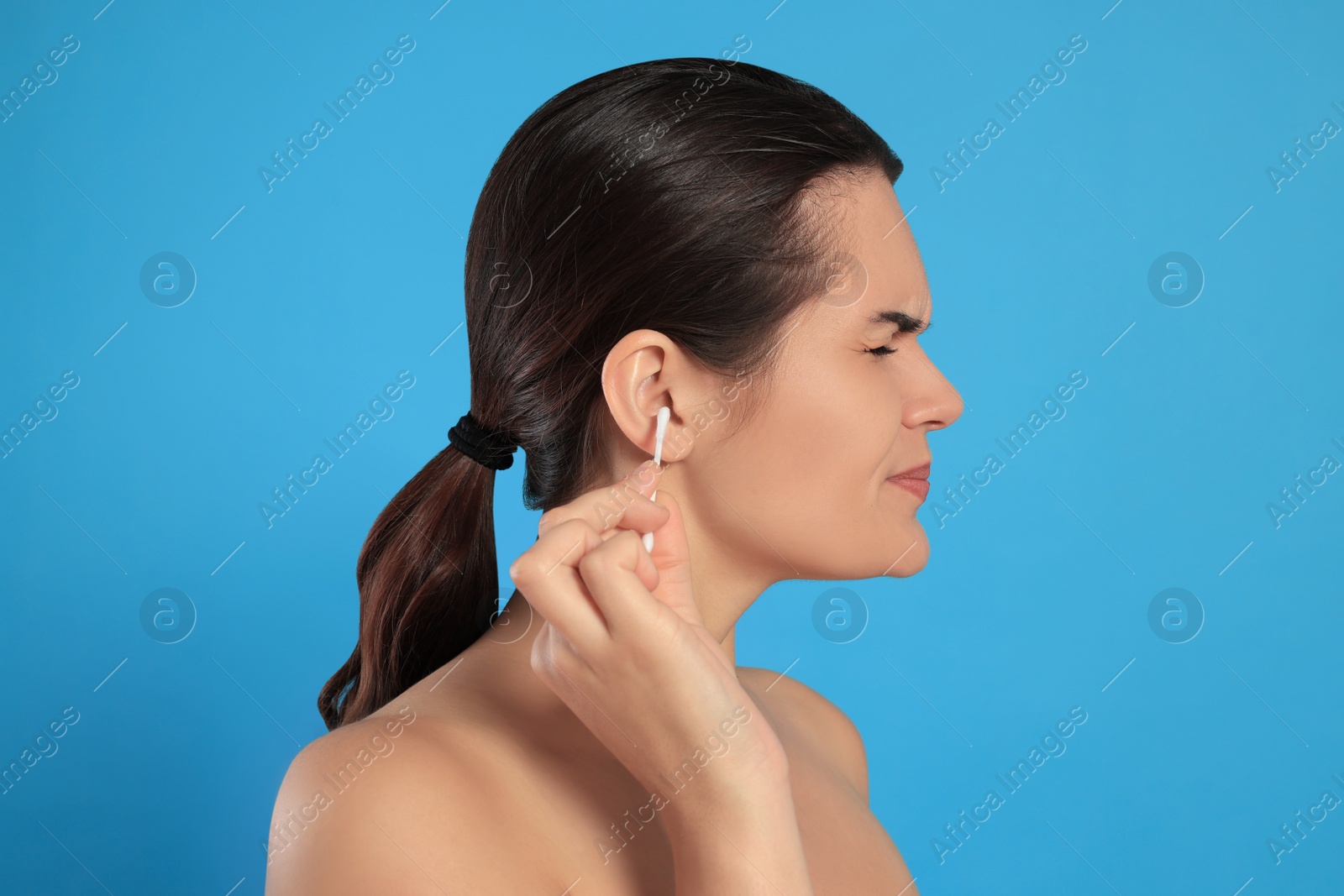 Photo of Young woman cleaning ear with cotton swab on light blue background