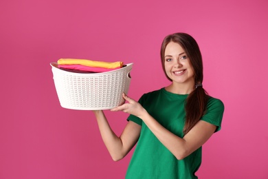 Photo of Happy young woman holding basket with laundry on color background