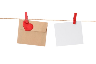 Photo of Blank card and envelope hanging on twine against white background. Valentine's Day celebration