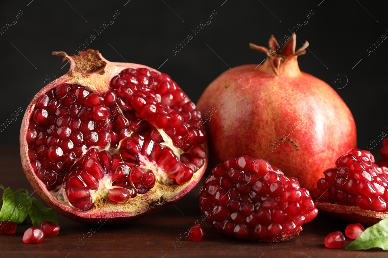 Photo of Fresh pomegranates and green leaves on wooden table, closeup