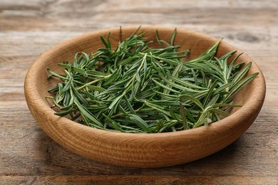 Photo of Fresh rosemary in bowl on wooden table, closeup