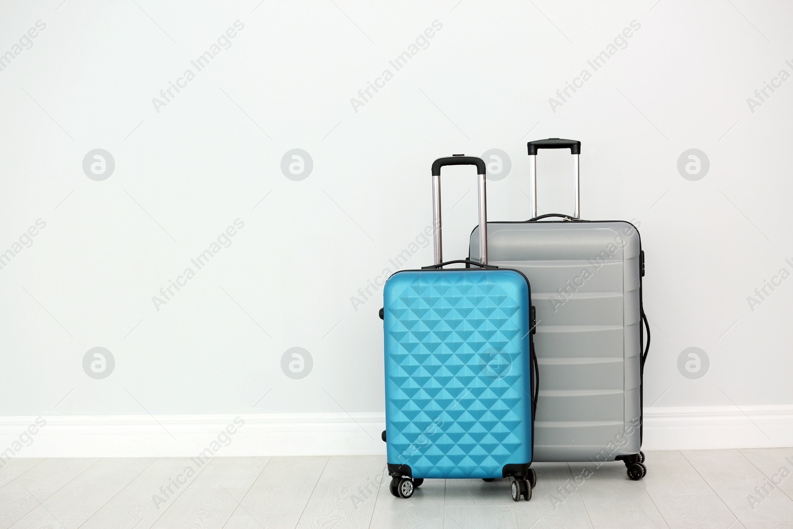 Photo of Modern suitcases on floor near light wall. Space for text