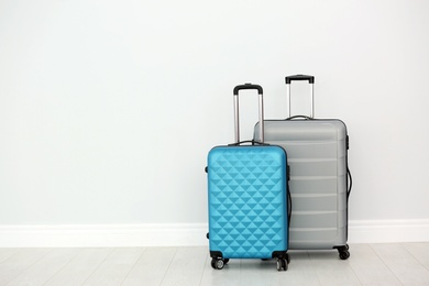 Photo of Modern suitcases on floor near light wall. Space for text