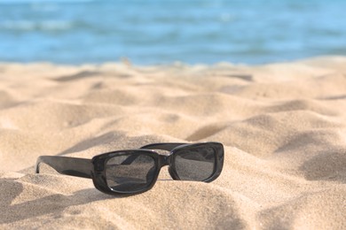 Photo of Stylish sunglasses on sandy beach near sea. Space for text
