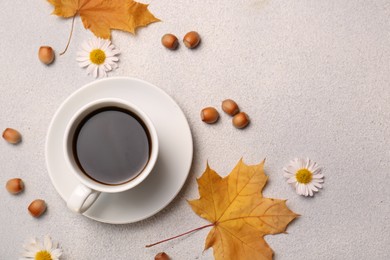 Flat lay composition with cup of hot drink and autumn leaves on light grey textured table. Space for text