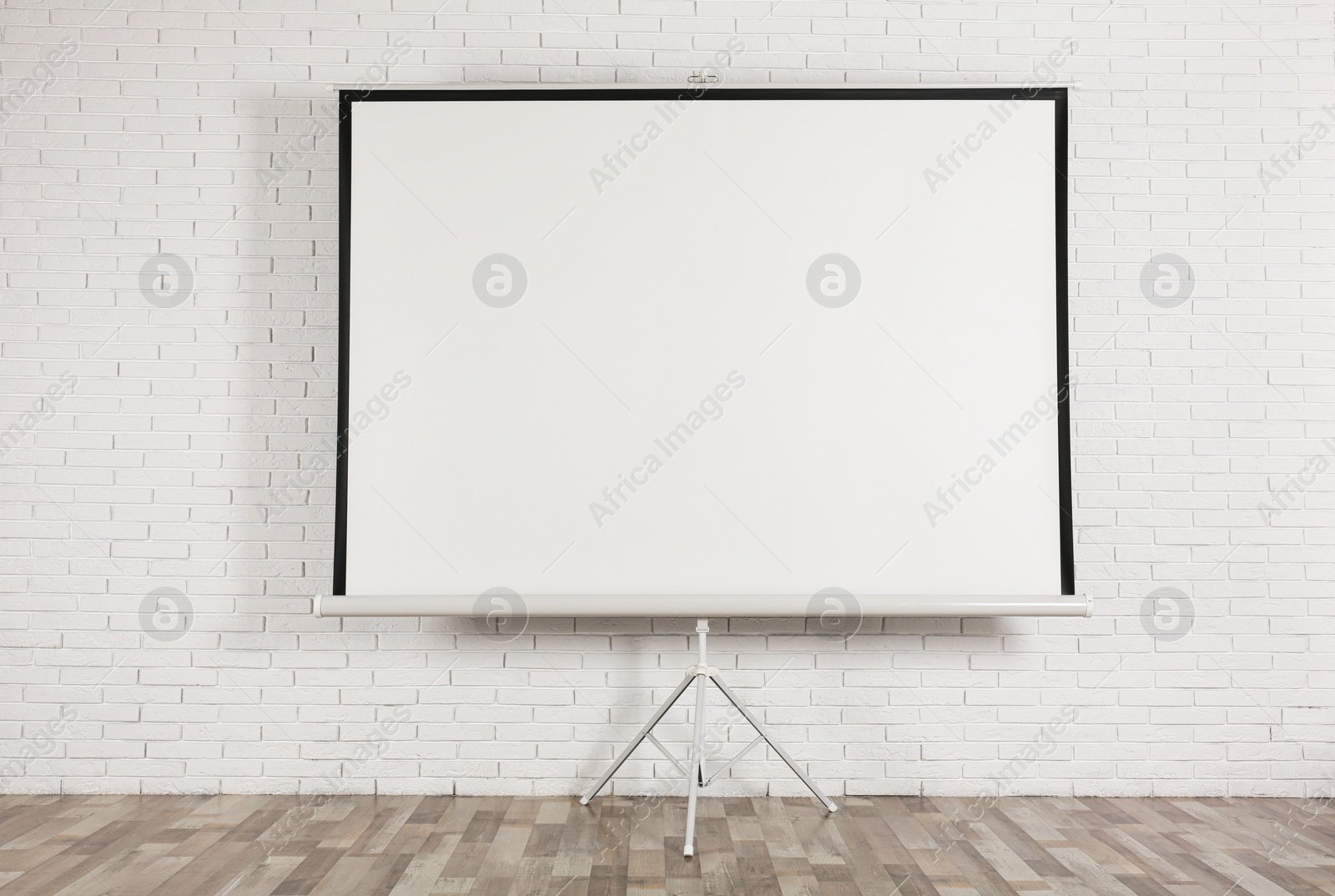 Photo of Blank projection screen near white brick wall indoors. Space for design