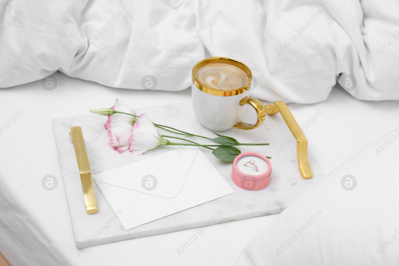 Photo of Tray with cup of coffee, flowers and beautiful engagement ring in box on white bed