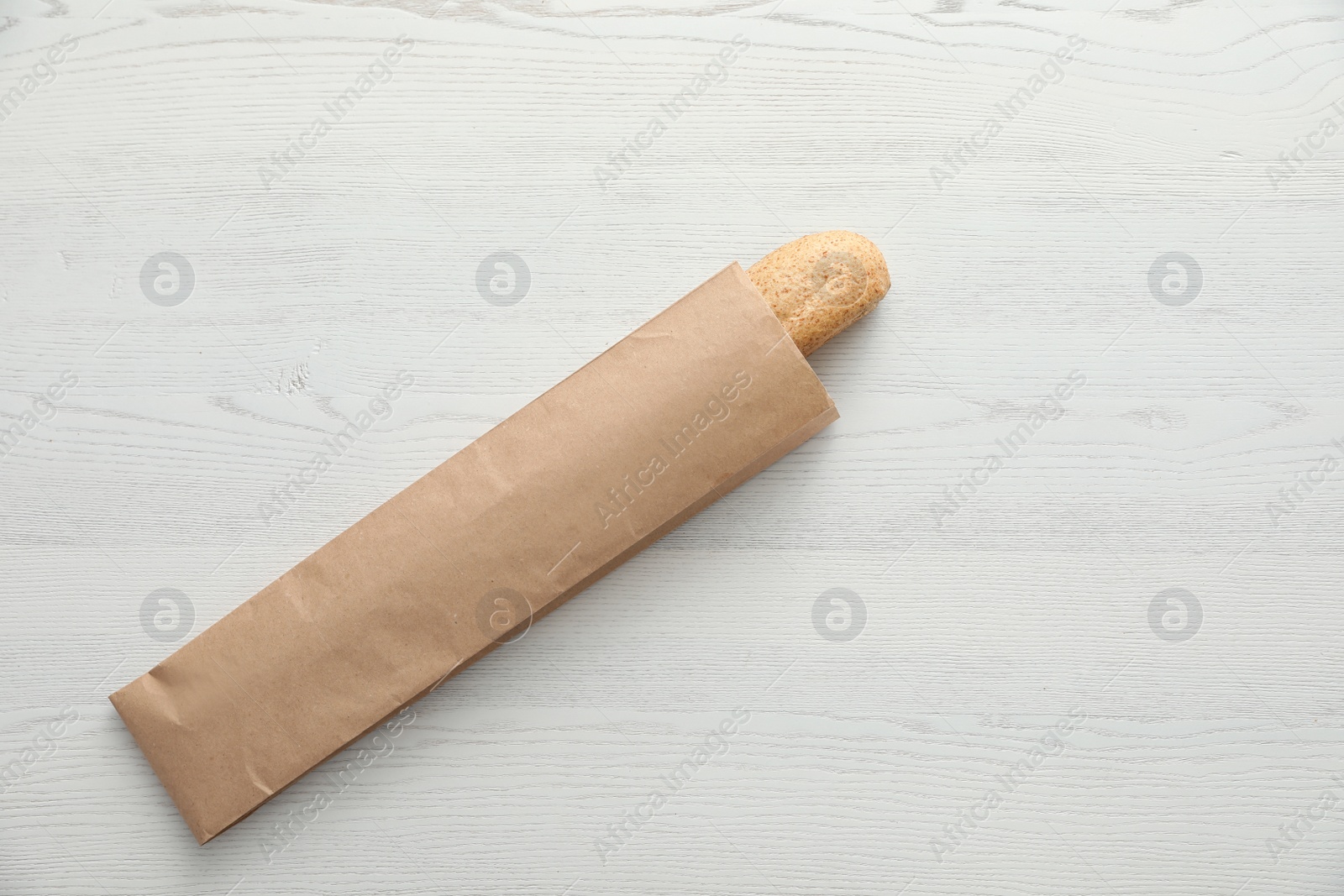 Photo of Baguette in paper bag on wooden table, top view with space for text