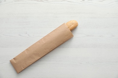 Baguette in paper bag on wooden table, top view with space for text