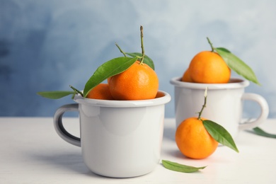 Photo of Fresh ripe tangerines with green leaves and mugs on table