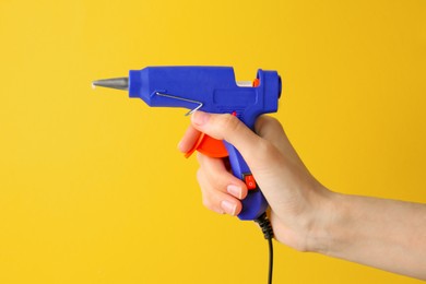 Photo of Woman holding empty blue glue gun on yellow background, closeup