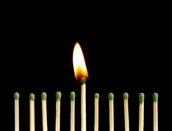 Burning match among unlit ones on black background, closeup