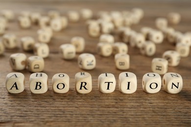 Photo of Word Abortion made of cubes on wooden table, closeup