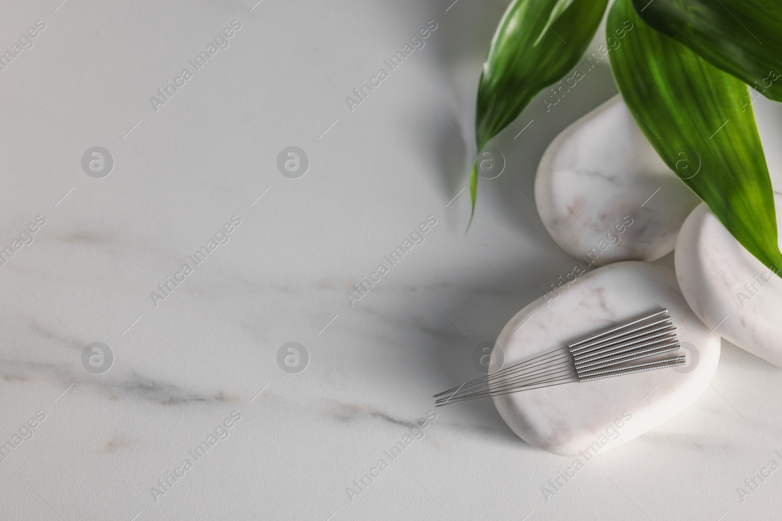 Photo of Acupuncture needles, spa stones and green leaves on white marble table, flat lay. Space for text