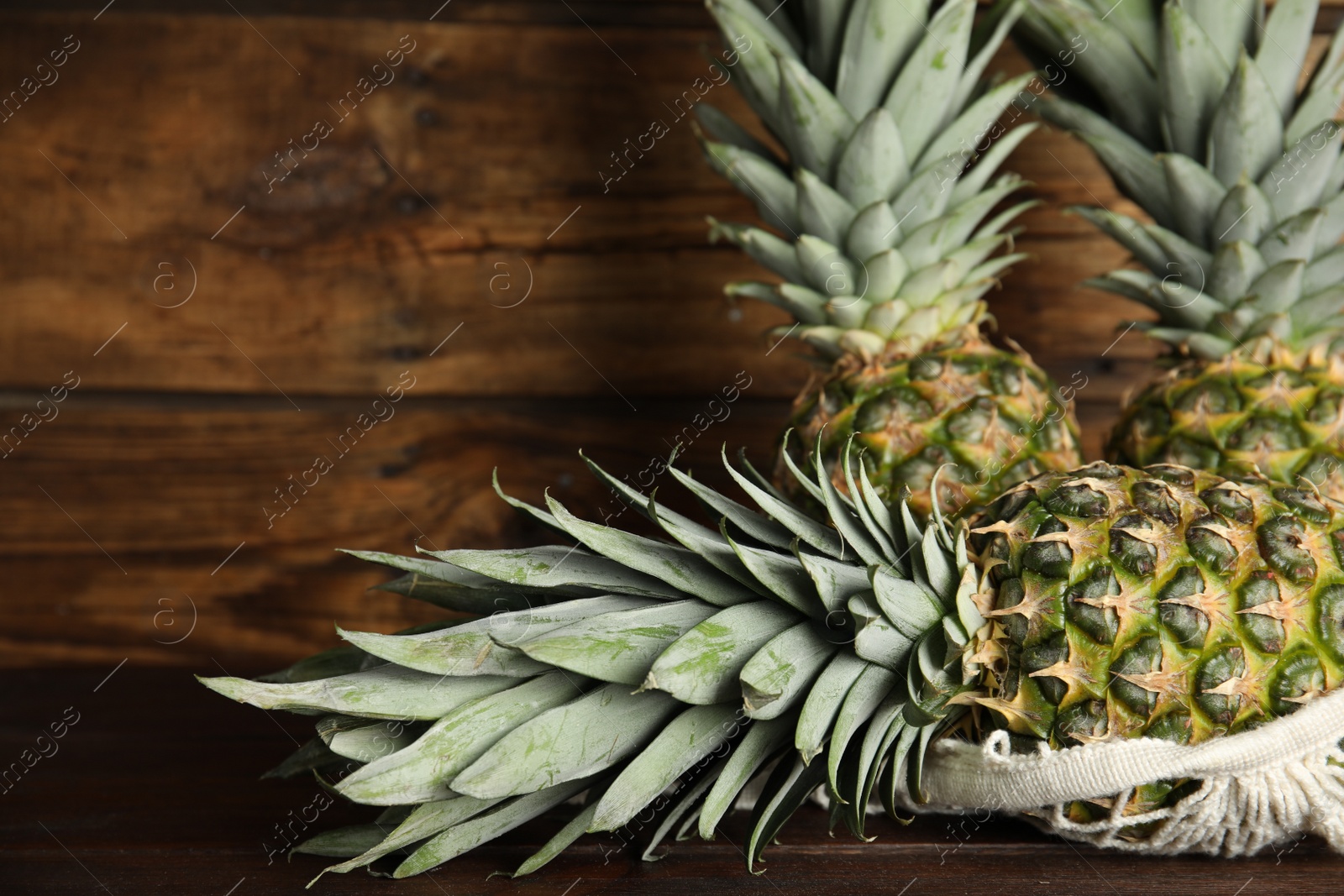 Photo of Bag with fresh juicy pineapples on wooden table, closeup