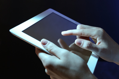 Photo of Woman using tablet on dark background, closeup