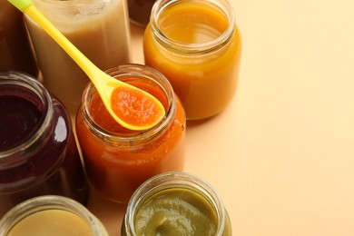 Jars with healthy baby food and spoon on beige background, closeup. Space for text