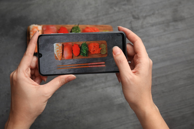 Blogger taking photo of sushi set at grey table, closeup