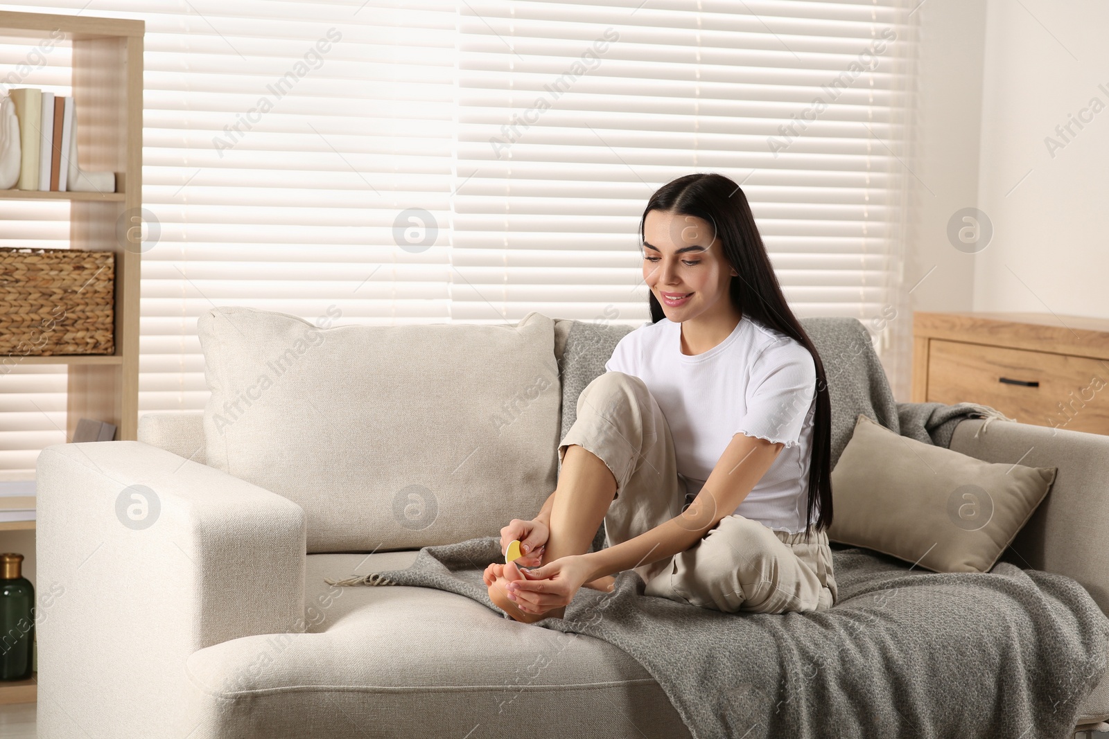 Photo of Beautiful young woman giving herself pedicure in living room