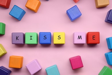 Colorful cubes with phrase Kiss Me on pink background, flat lay