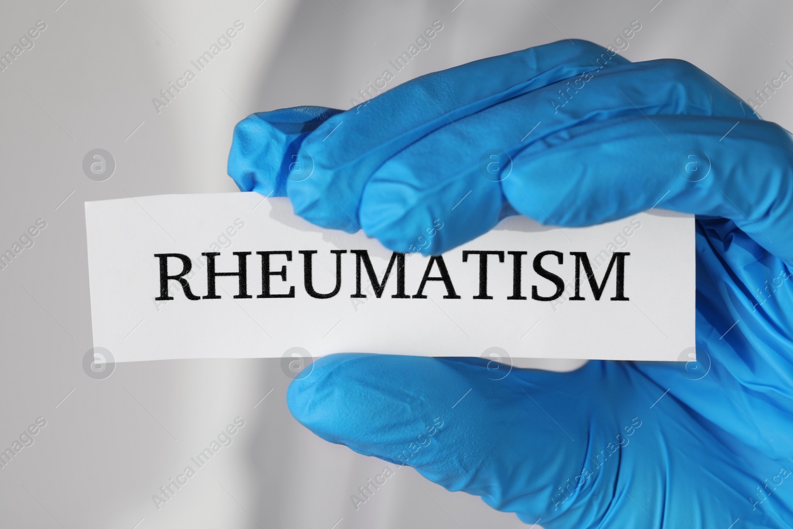 Photo of Doctor in glove holding sheet of paper with word Rheumatism, closeup