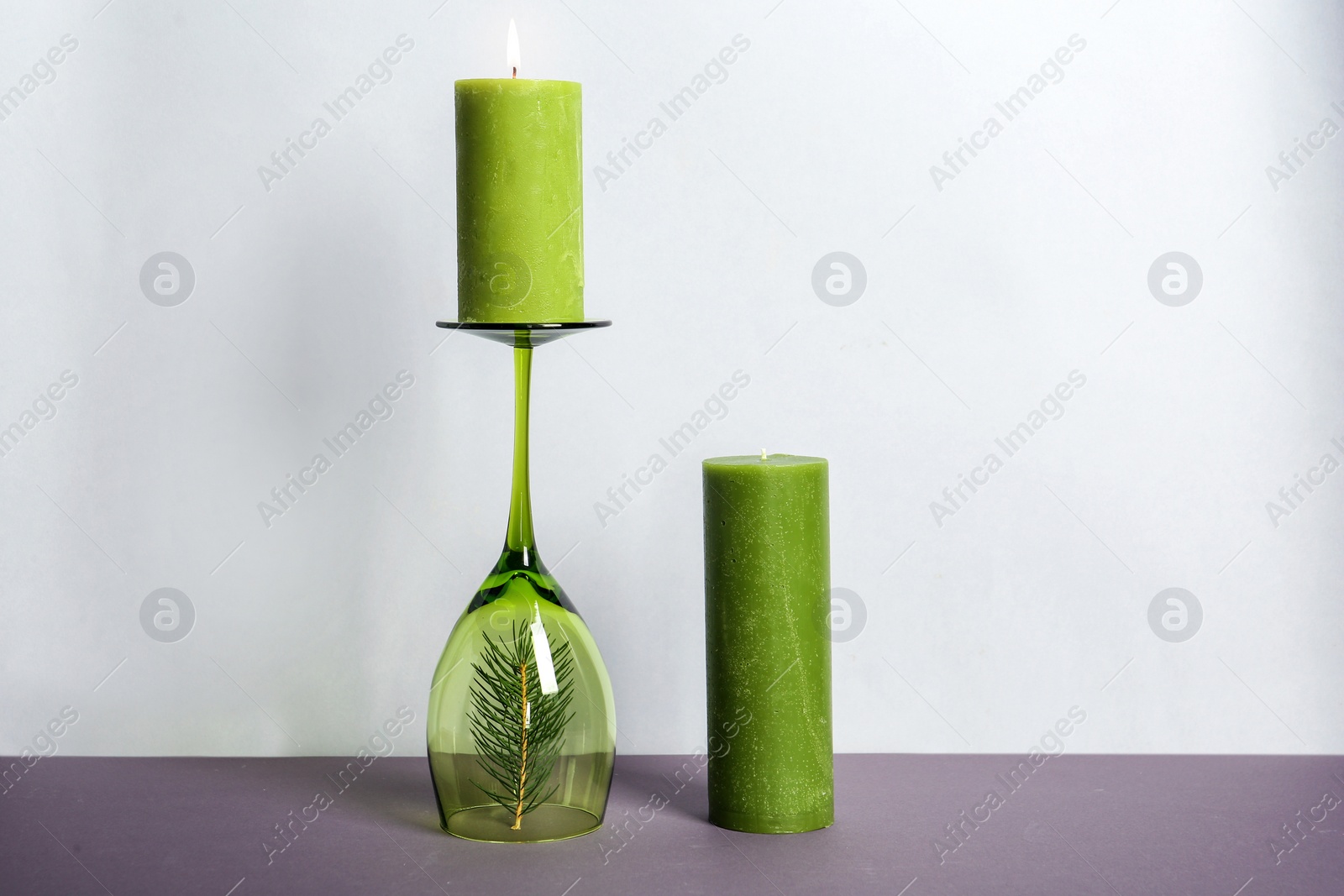 Photo of Decorative wax candles and wineglass on table against light background