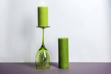 Photo of Decorative wax candles and wineglass on table against light background