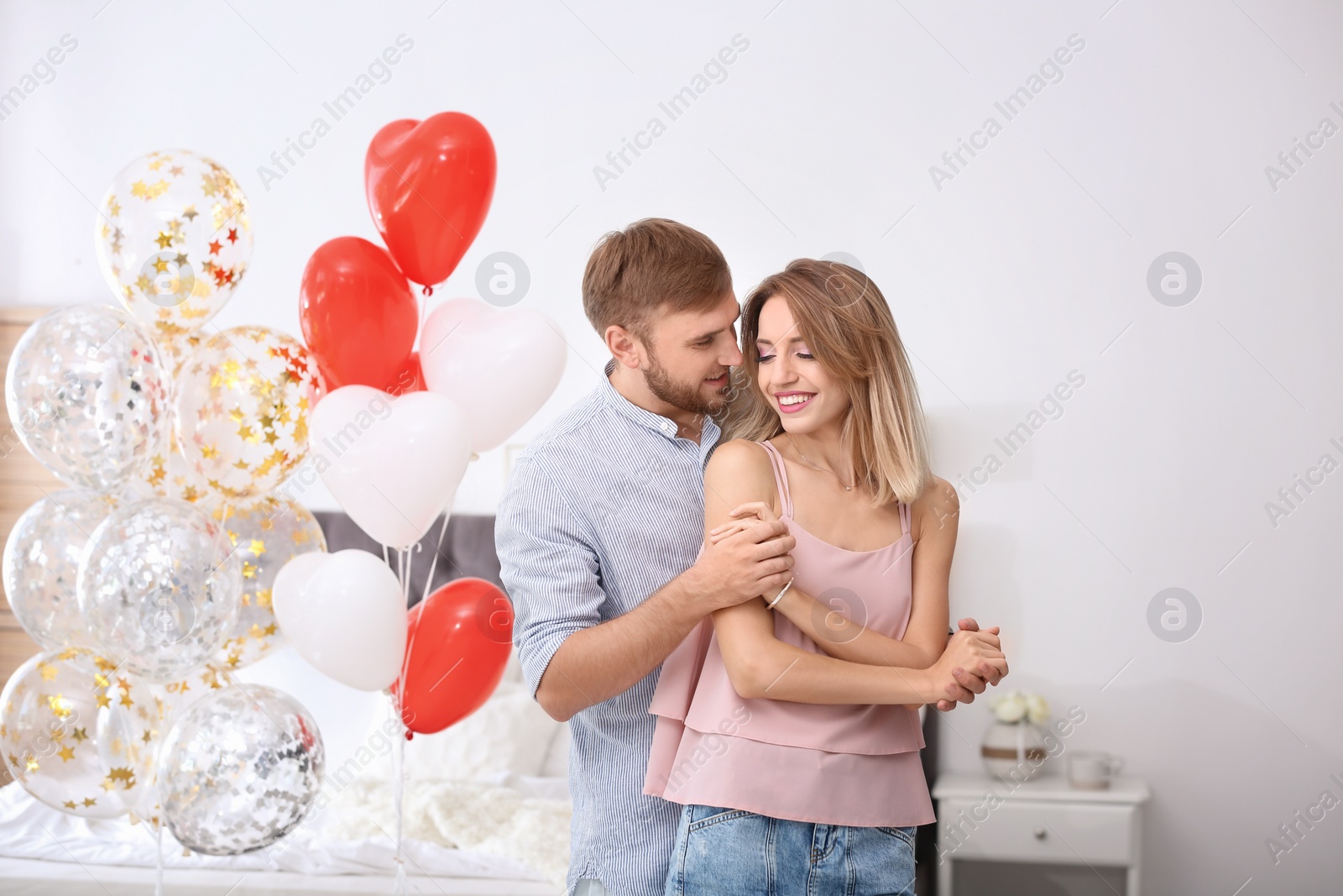 Photo of Young couple with air balloons in bedroom. Celebration of Saint Valentine's Day