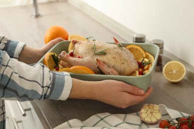 Photo of Woman holding baking pan with Chicken and orange slices at countertop, closeup