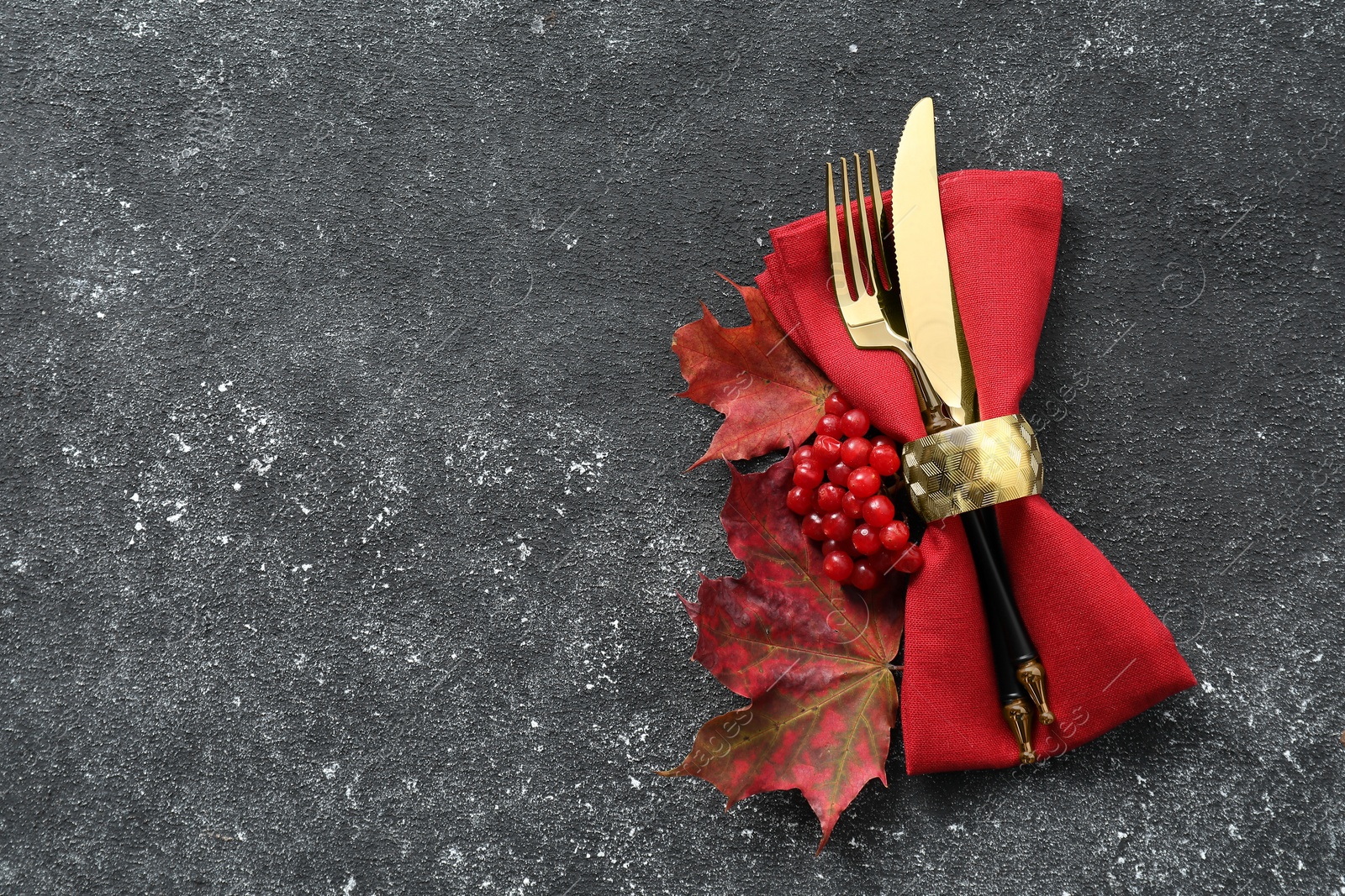 Photo of Thanksgiving table setting. Cutlery, napkin, autumn leaves and berries on black background, flat lay with space for text