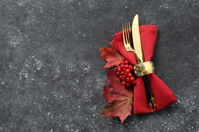 Photo of Thanksgiving table setting. Cutlery, napkin, autumn leaves and berries on black background, flat lay with space for text