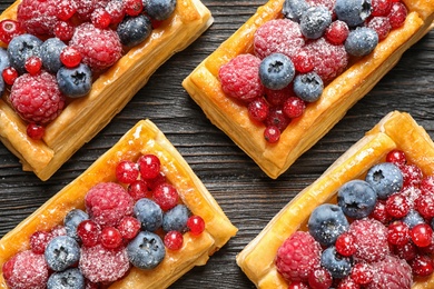 Photo of Fresh delicious puff pastry with sweet berries on dark wooden table, flat lay