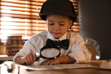 Cute little detective exploring fingerprints with magnifying glass at table in office