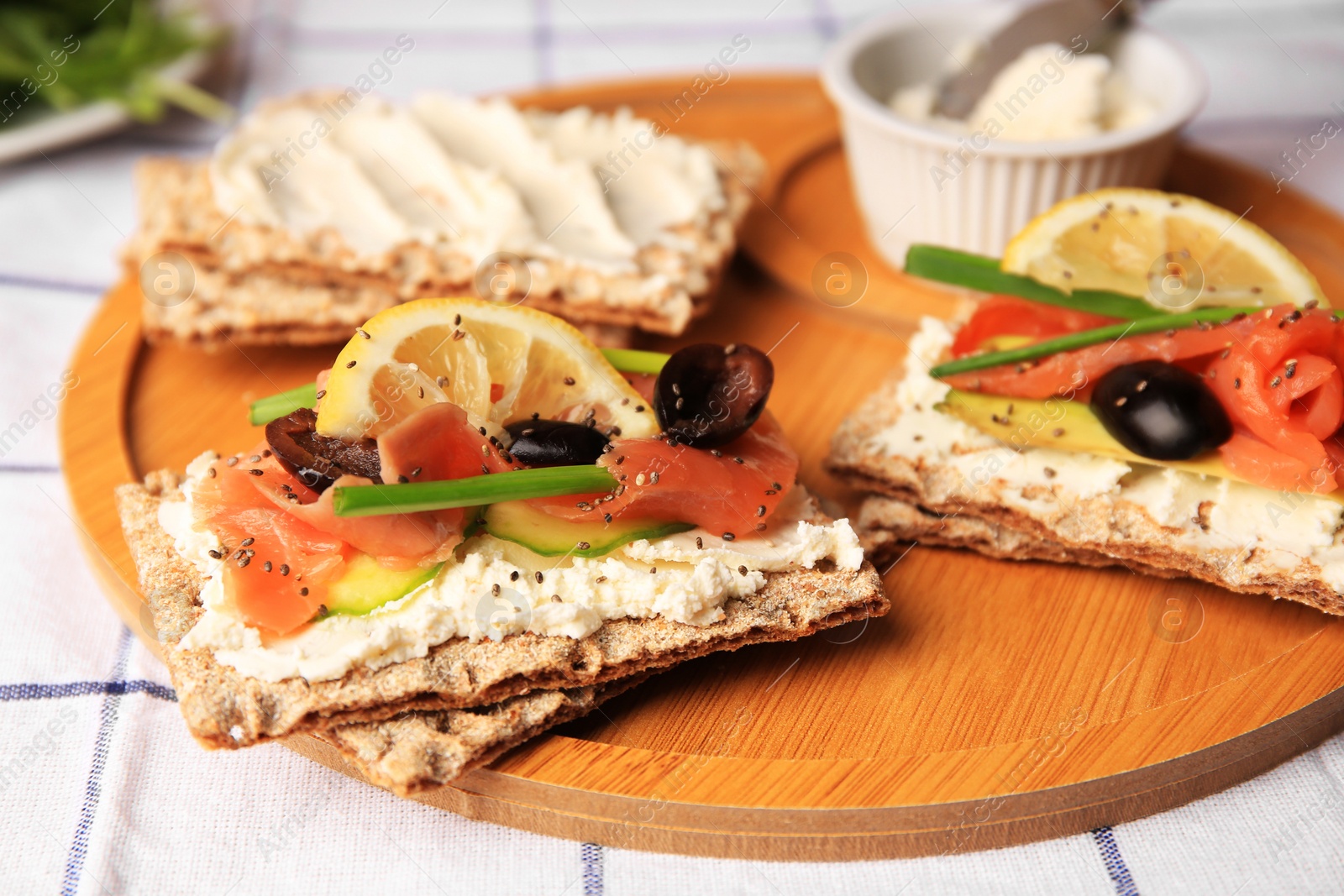 Photo of Fresh crunchy crispbreads with cream cheese, salmon, olives, lemon and green onion on table, closeup