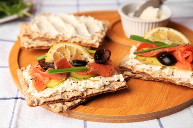 Photo of Fresh crunchy crispbreads with cream cheese, salmon, olives, lemon and green onion on table, closeup