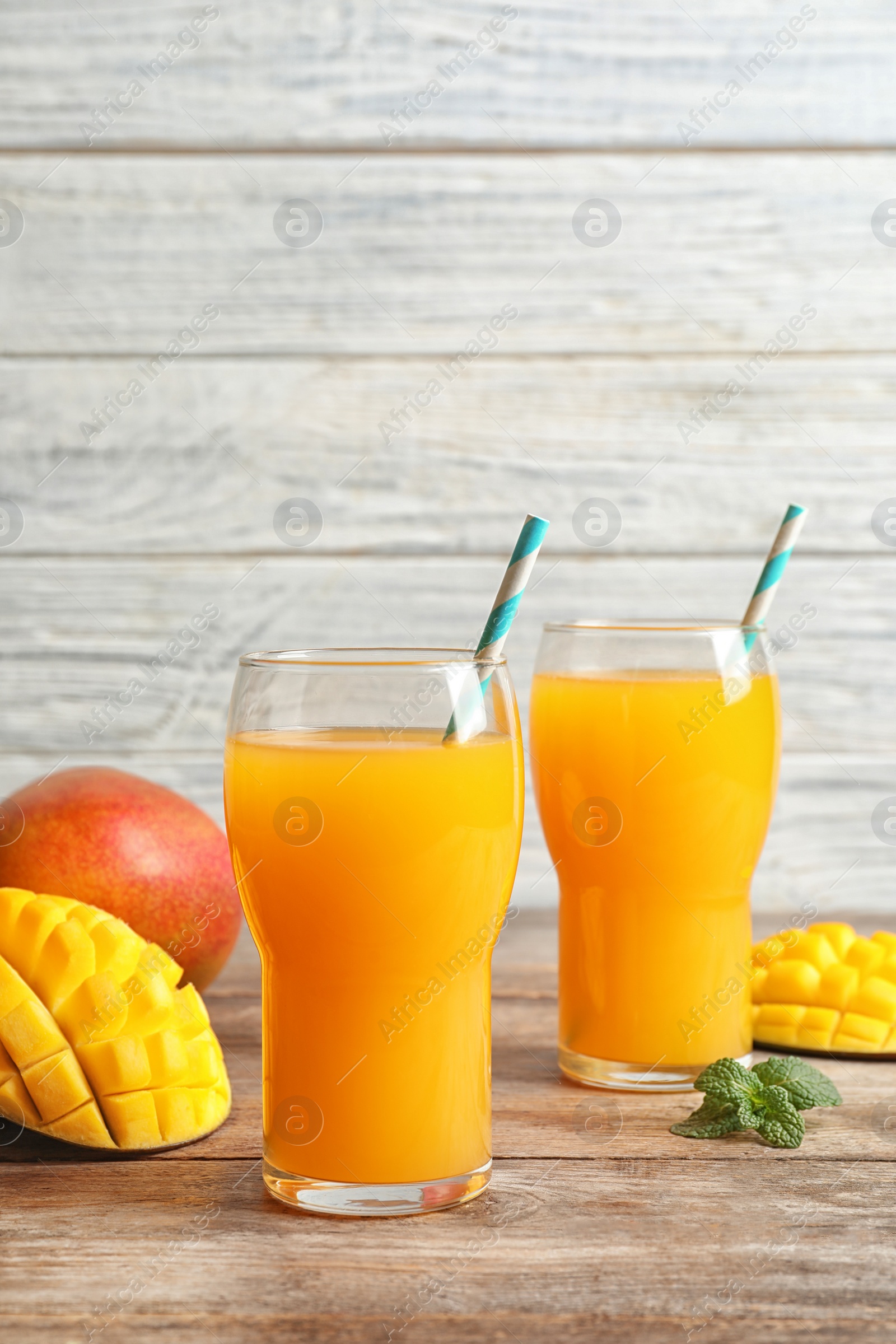 Photo of Fresh tropical mango juice and fruits on wooden table. Space for text