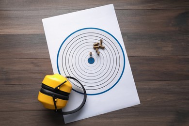 Photo of Shooting target, headphones and bullets on wooden table, top view