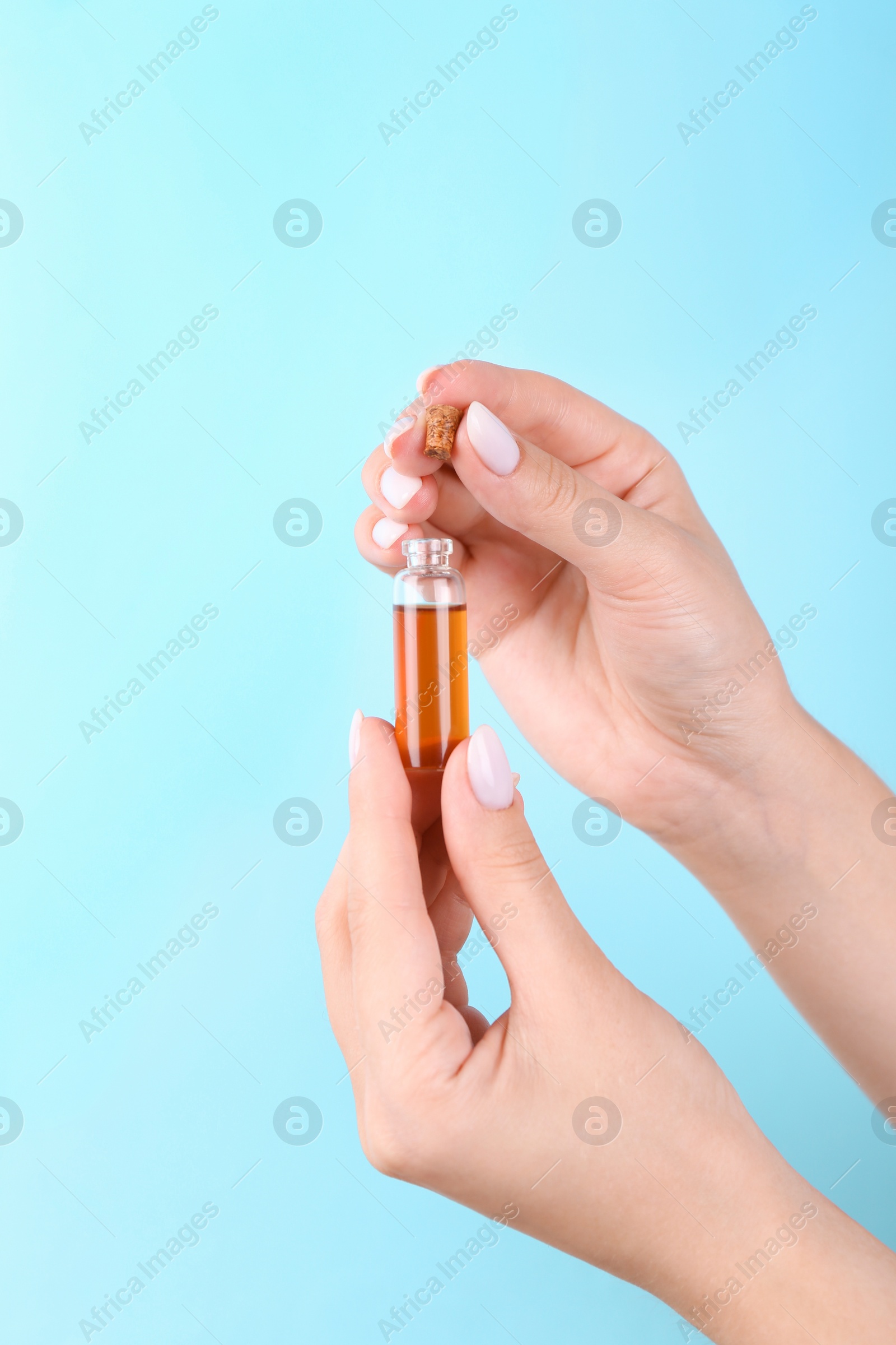 Photo of Woman holding bottle of essential oil on light blue background, closeup