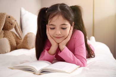 Photo of Little girl reading book on bed at home