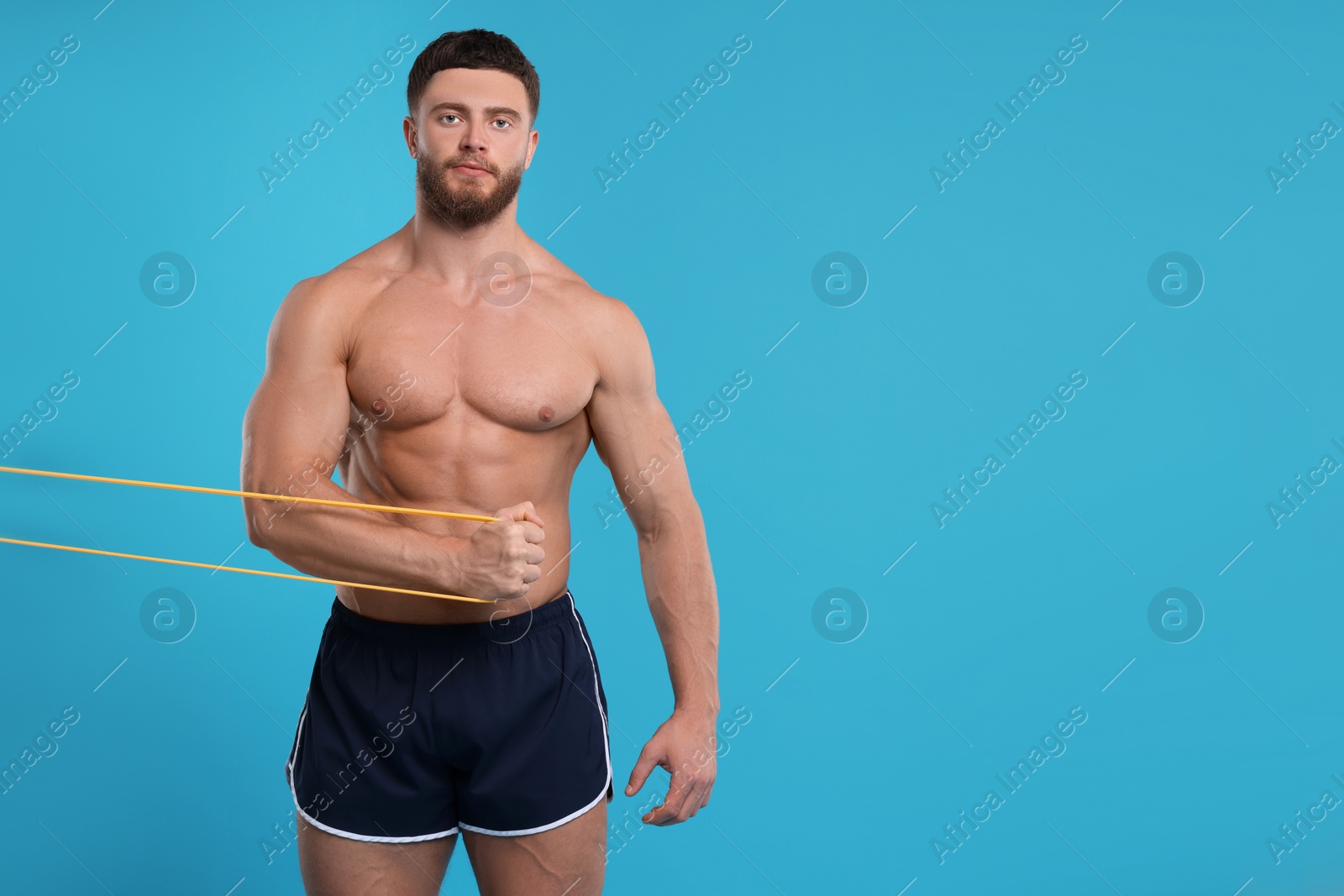 Photo of Young man exercising with elastic resistance band on light blue background. Space for text