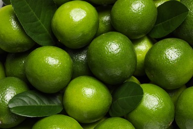 Photo of Fresh ripe limes and leaves as background, top view