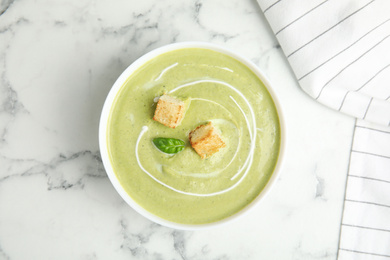 Photo of Delicious broccoli cream soup with croutons served on white marble table, top view