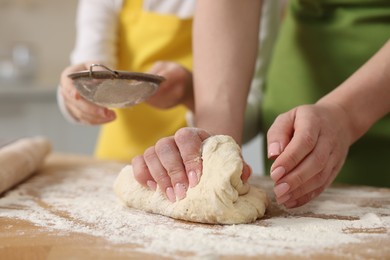 Making bread. Mother and her daughter kneading dough at wooden table in kitchen, closeup