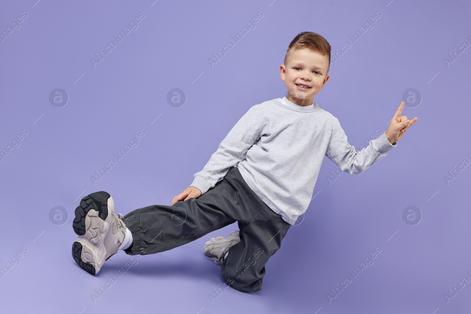 Photo of Happy little boy dancing on violet background