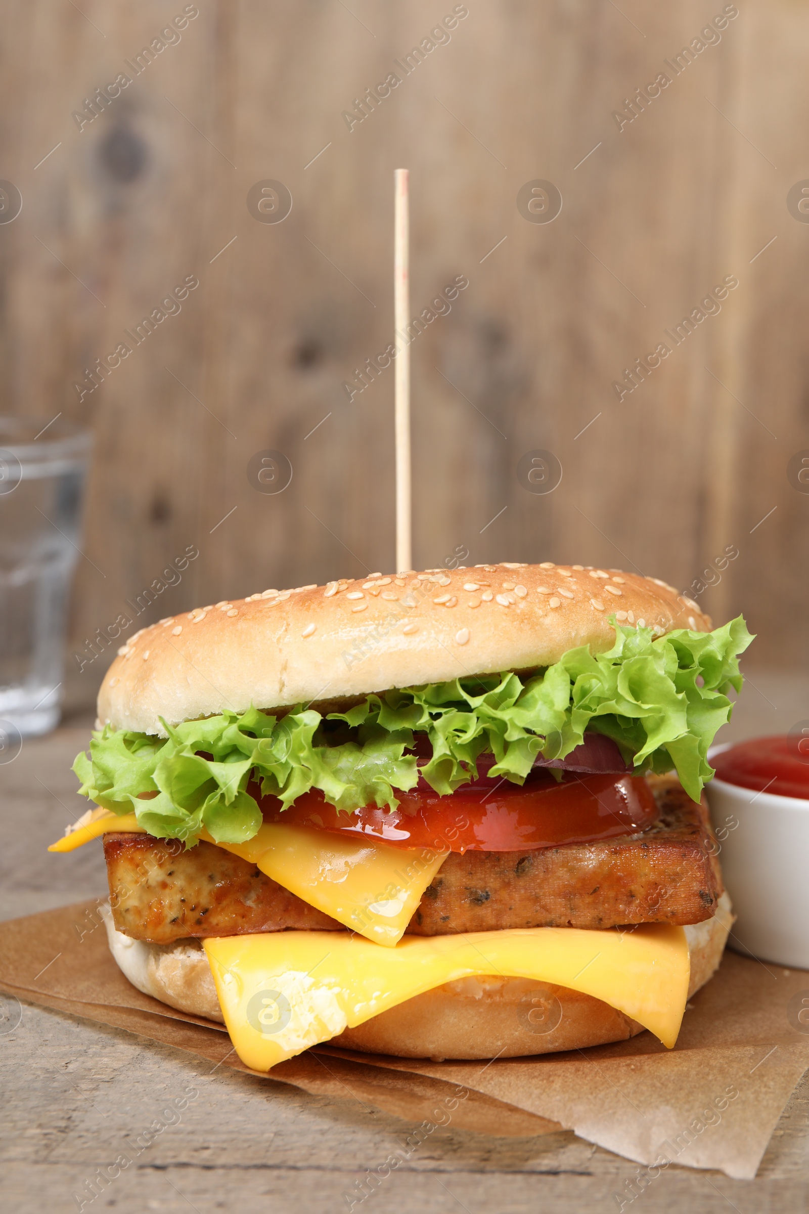 Photo of Delicious burger with tofu, fresh vegetables and sauce on wooden table