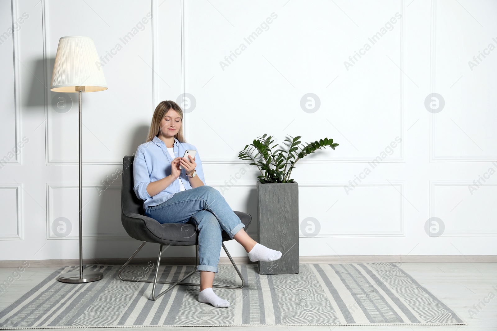 Photo of Young woman with phone sitting in armchair at home, space for text. Interior design