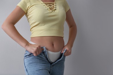 Woman trying to put on tight jeans against light grey background, closeup