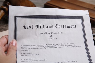 Photo of Woman holding last will and testament at table, closeup